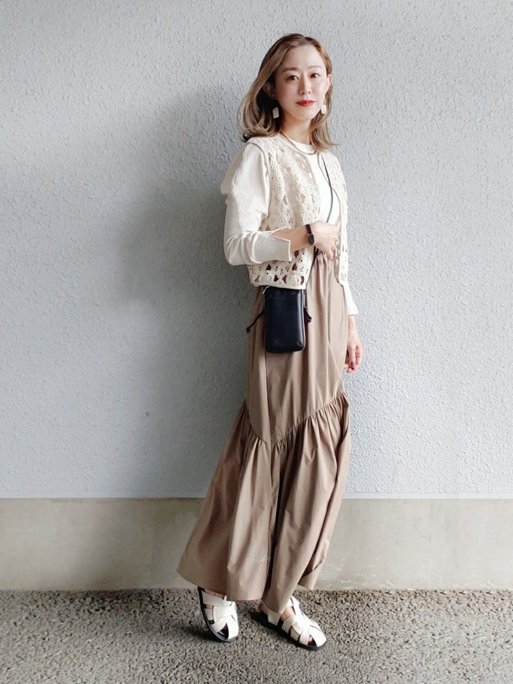 ブラック系のベスト、ホワイト系のワンピース、ブラック系の財布を着用したレディースの春コーディネートの4枚目の写真