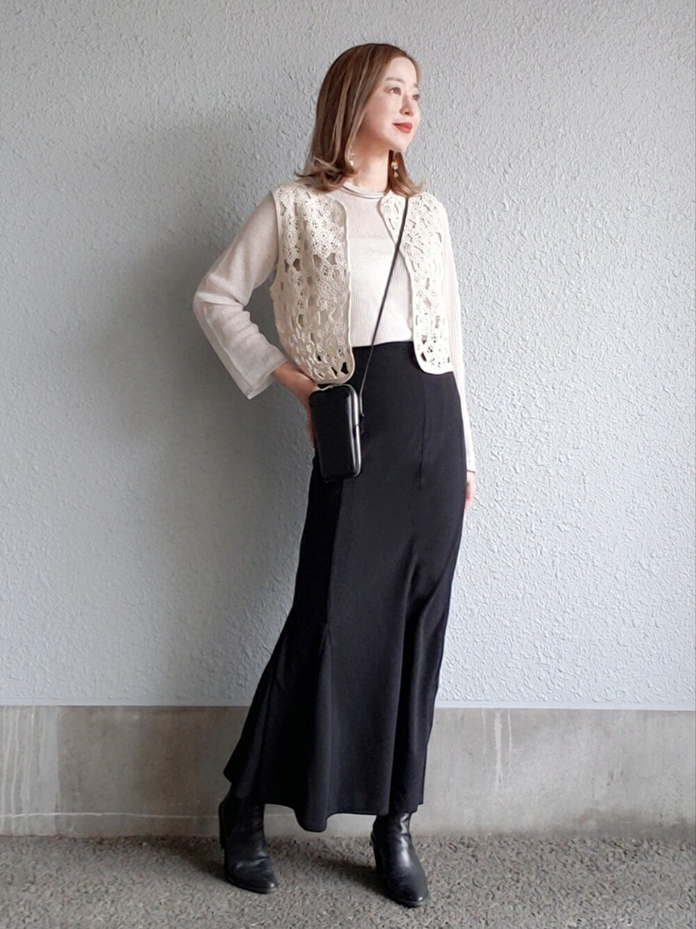 ブラック系のスカート、ホワイト系のベスト、ブラック系のブーツを着用したレディースの春コーディネートの2枚目の写真