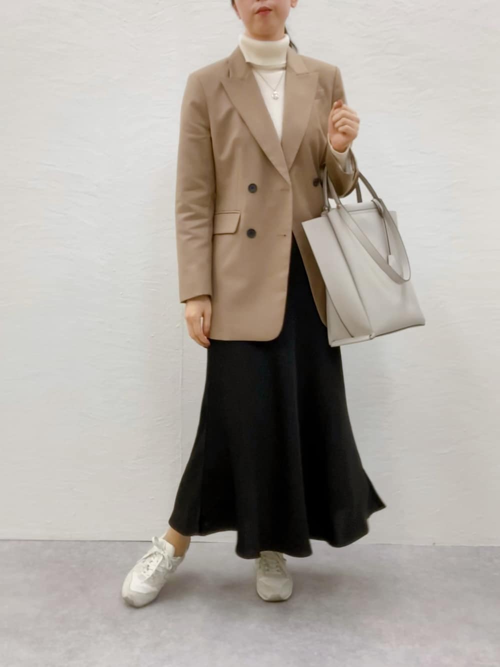 グレー系のトートバッグ、ブラック系のスカート、ホワイト系のスニーカーを着用したレディースの秋コーディネートの1枚目の写真