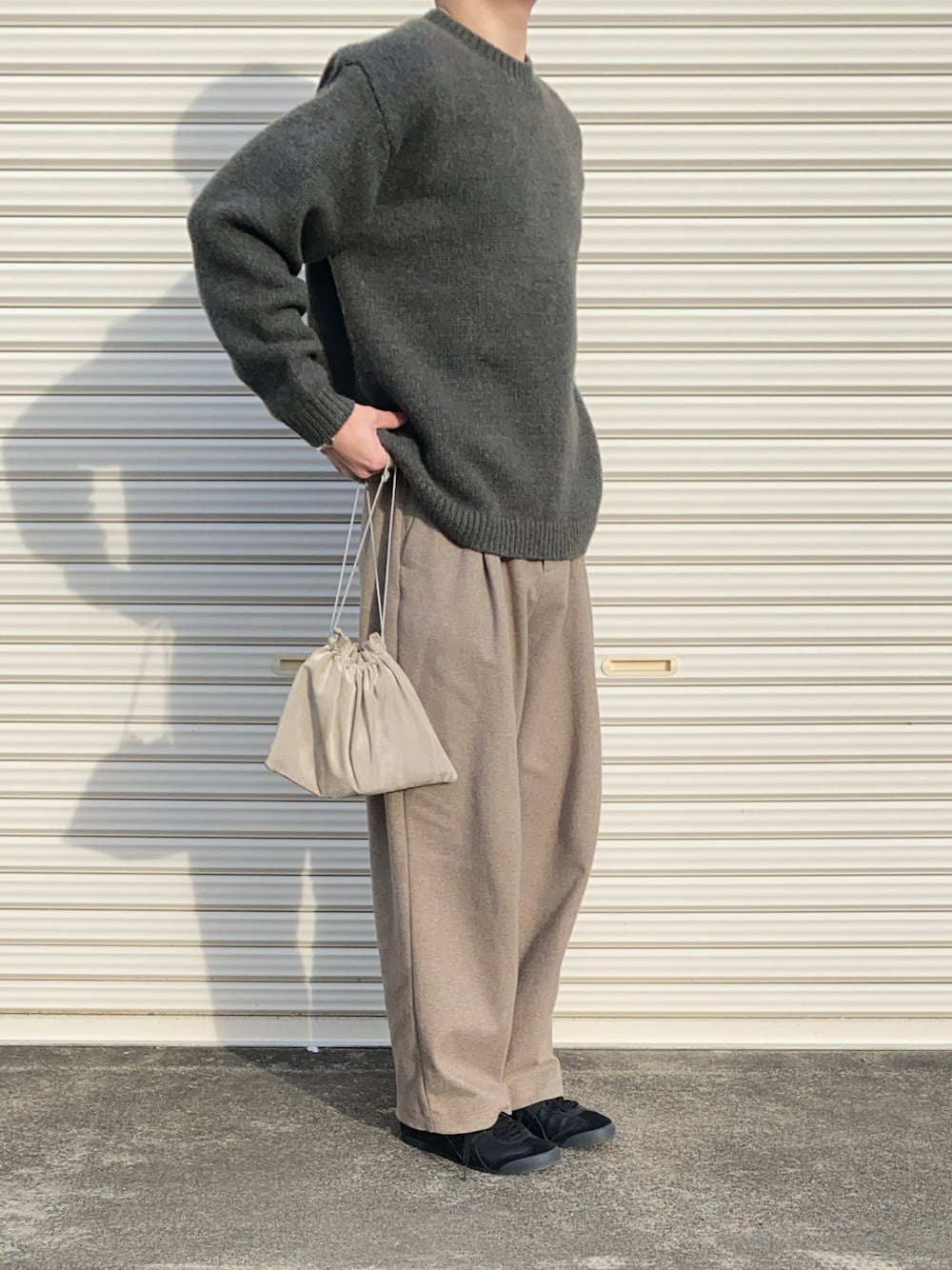 ベージュ系のショルダーバッグ、グリーン系のニット/セーター、ベージュ系のスラックスを着用したメンズの冬コーディネートの1枚目の写真