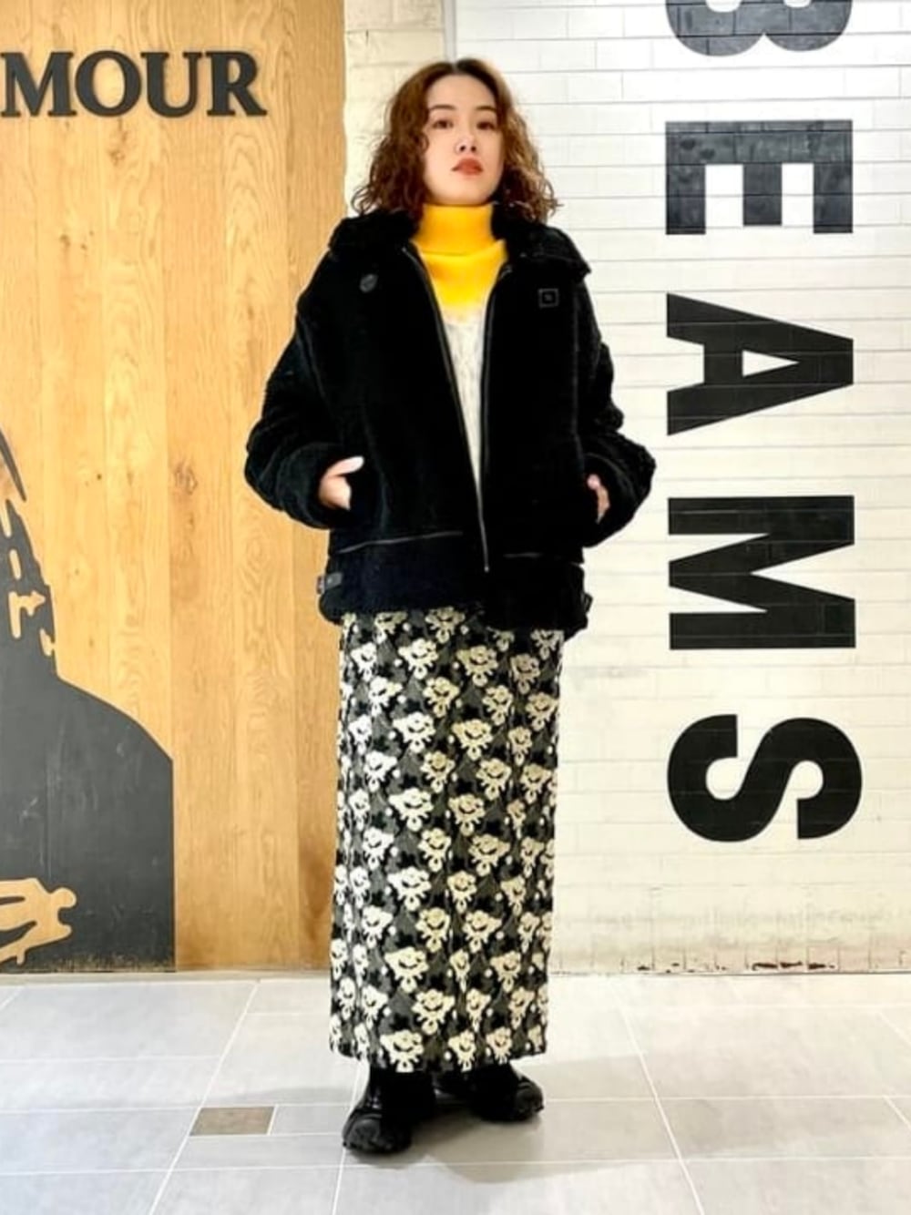 グレー系のスカート、グレー系のベスト、ブラック系のブルゾンを着用したレディースの冬コーディネートの1枚目の写真