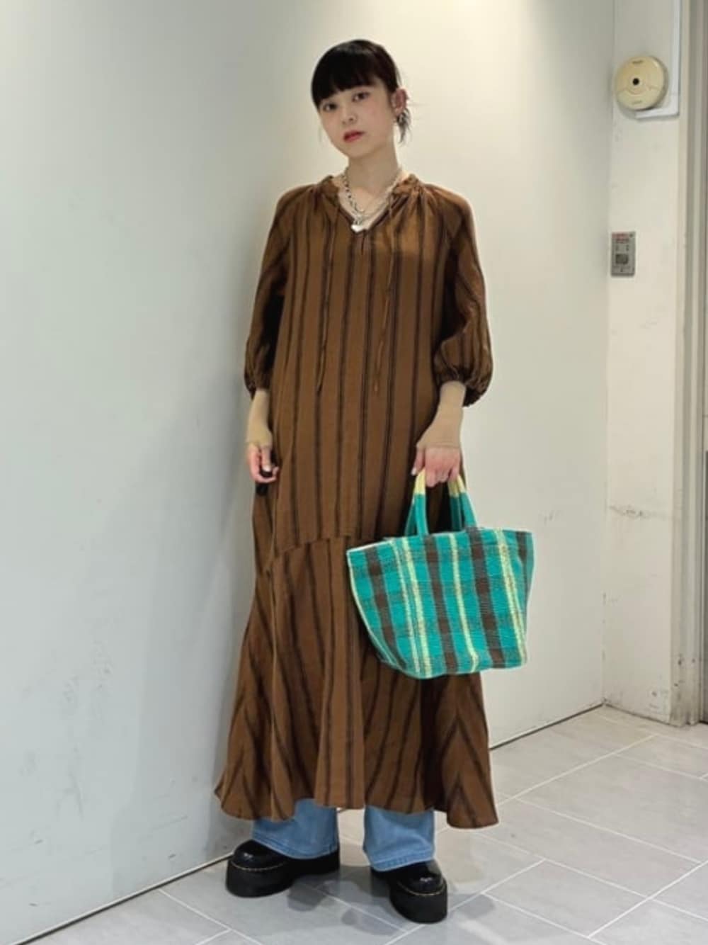 ブラウン系のワンピース、ブルー系のデニムパンツ、グリーン系のトートバッグを着用したレディースの夏コーディネートの1枚目の写真