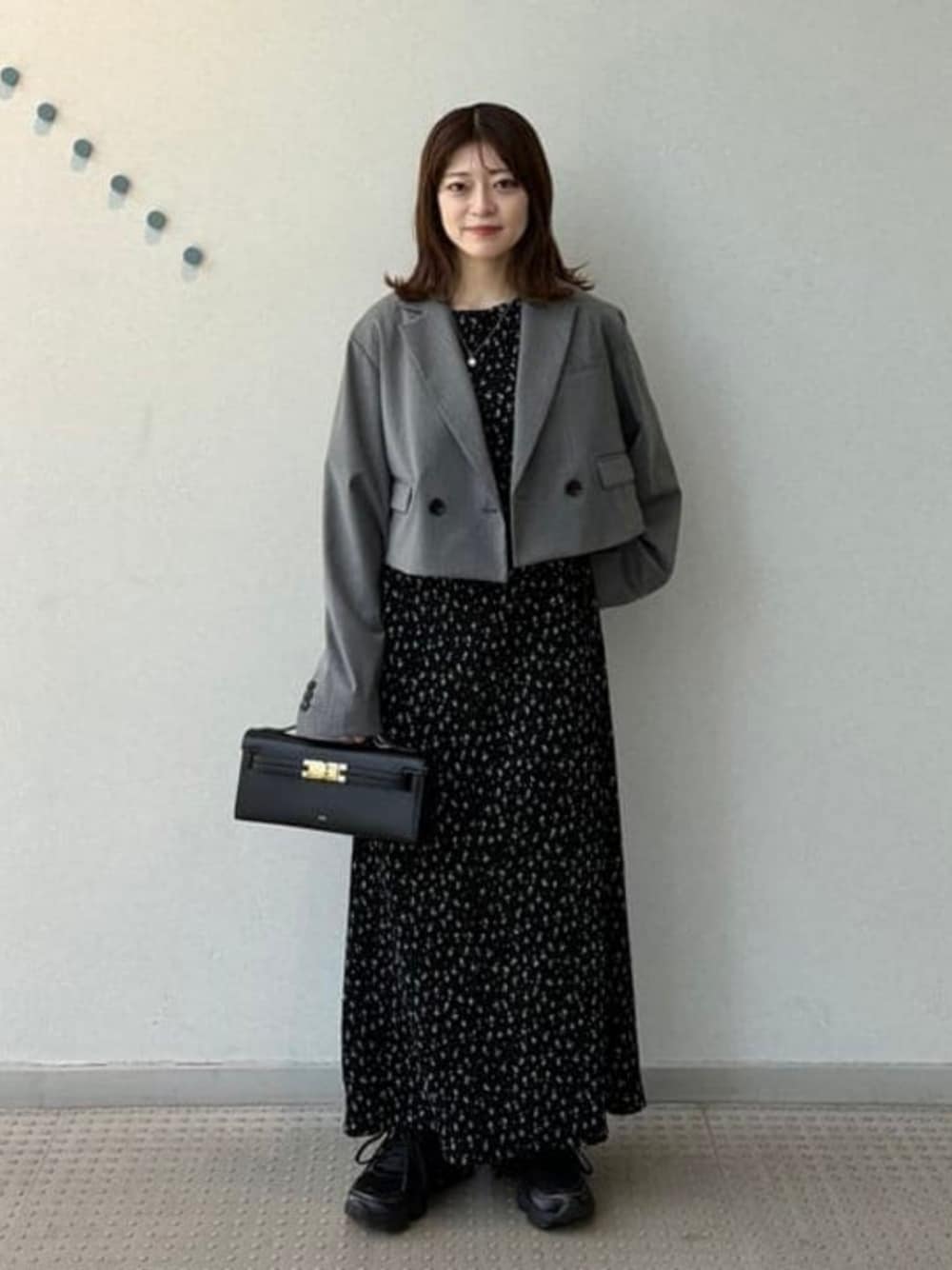 グレー系のテーラードジャケット、ブラック系のワンピース、グレー系のスニーカーを着用したレディースの春コーディネートの1枚目の写真