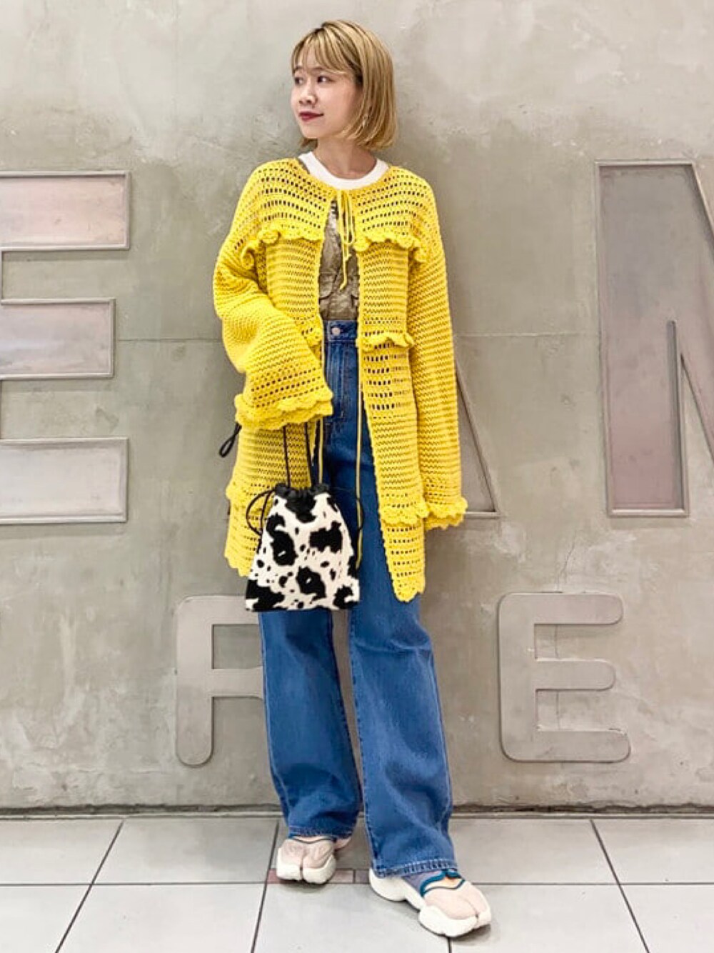 ブラック系のショルダーバッグ、イエロー系のカーディガン/ボレロ、ブルー系のデニムパンツを着用したレディースの秋コーディネートの1枚目の写真