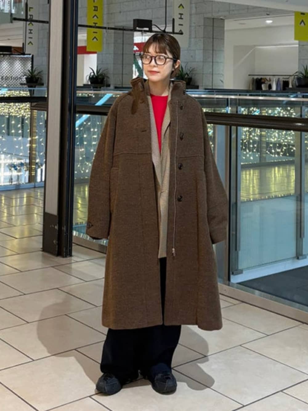 ブラウン系のステンカラーコート、ブラウン系のテーラードジャケット、レッド系のニット/セーターを着用したレディースの冬コーディネートの1枚目の写真