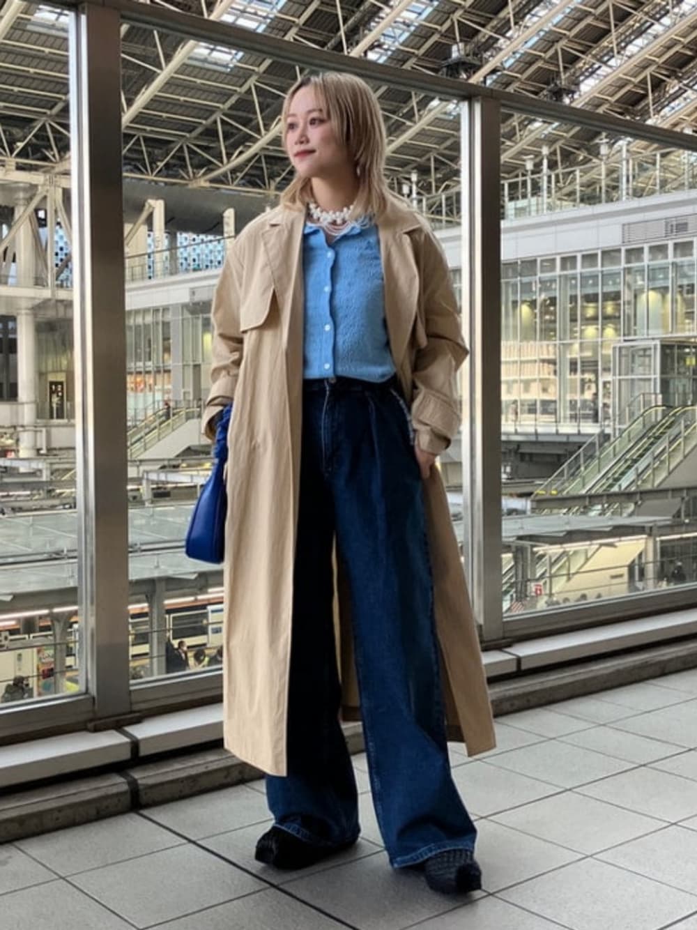 ブルー系のメッセンジャーバッグ、ブルー系のシャツ/ブラウス、ベージュ系のトレンチコートを着用したレディースの冬コーディネートの1枚目の写真