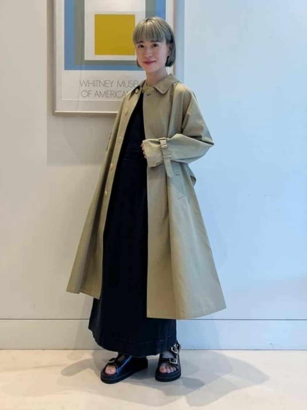 ベージュ系のステンカラーコート、ブラック系のワンピースを着用したレディースの春コーディネートの1枚目の写真