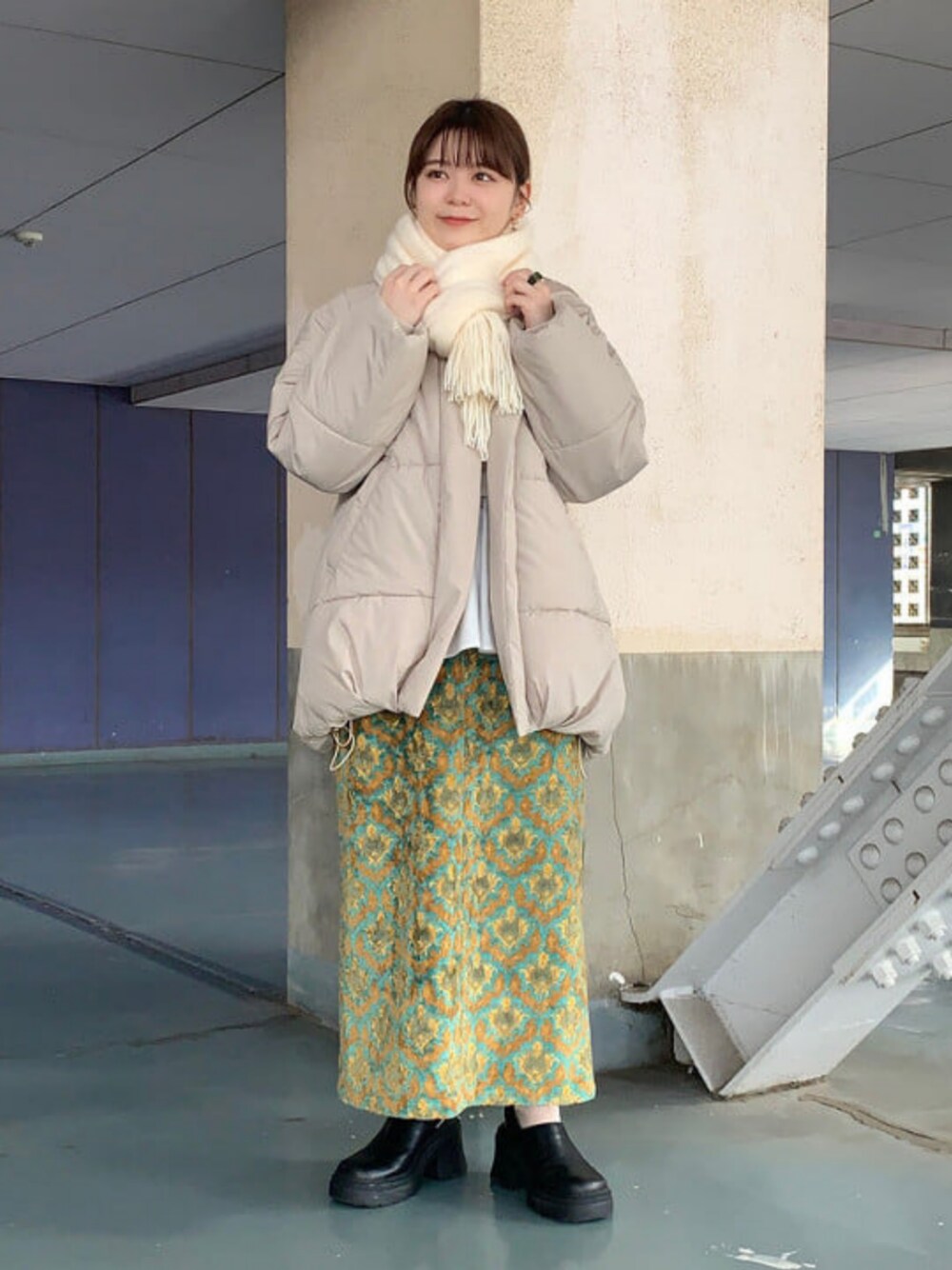 イエロー系のスカート、ベージュ系のダウンジャケット/コート、ホワイト系のマフラーを着用したレディースの秋コーディネートの1枚目の写真