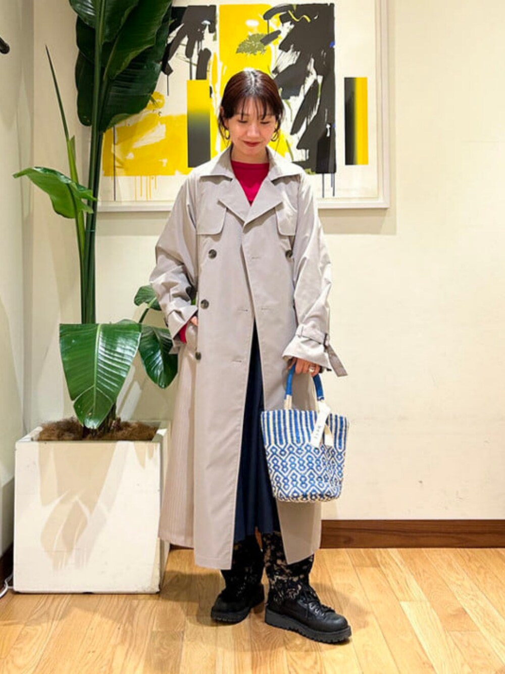 ブルー系のかごバッグ、シルバー系のトレンチコートを着用したレディースの春コーディネートの1枚目の写真