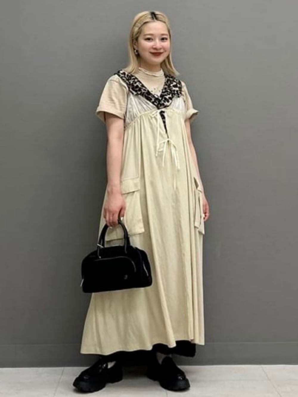 ブラック系のハンドバッグ、ベージュ系のTシャツ/カットソー、ベージュ系のワンピースを着用したレディースの春コーディネートの1枚目の写真