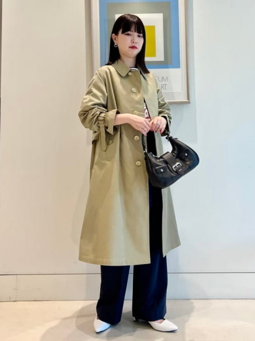 ブルー系のスラックス、ブラック系のハンドバッグ、ベージュ系のステンカラーコートを着用したレディースの冬コーディネートの1枚目の写真