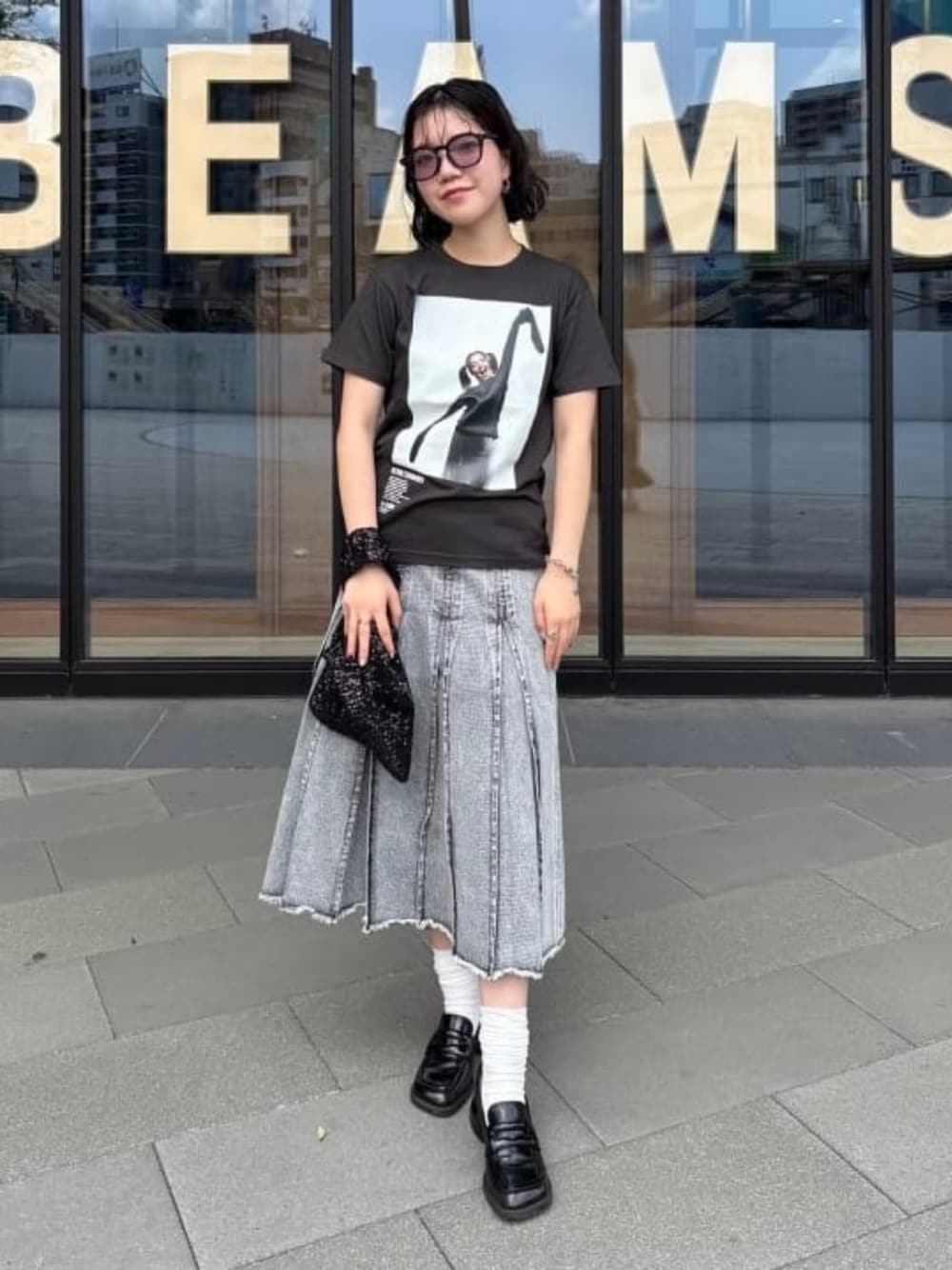 グレー系のデニムスカート、ブラック系のTシャツ/カットソー、ブラック系のトートバッグを着用したレディースの夏コーディネートの1枚目の写真