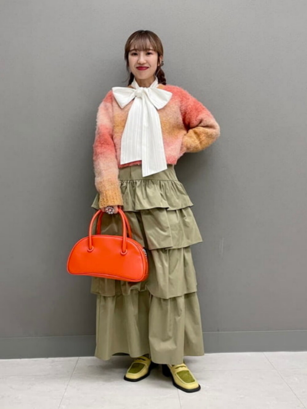 オレンジ系のボストンバッグ、オレンジ系のニット/セーター、ブラウン系のスカートを着用したレディースの秋コーディネートの1枚目の写真