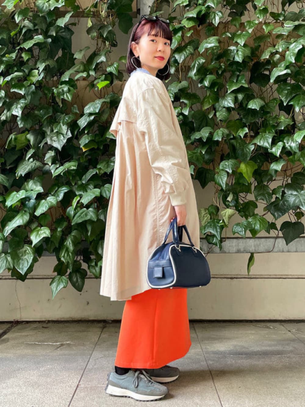 ブルー系のトートバッグ、ベージュ系のノーカラーコート、オレンジ系のスカートを着用したレディースの春コーディネートの1枚目の写真