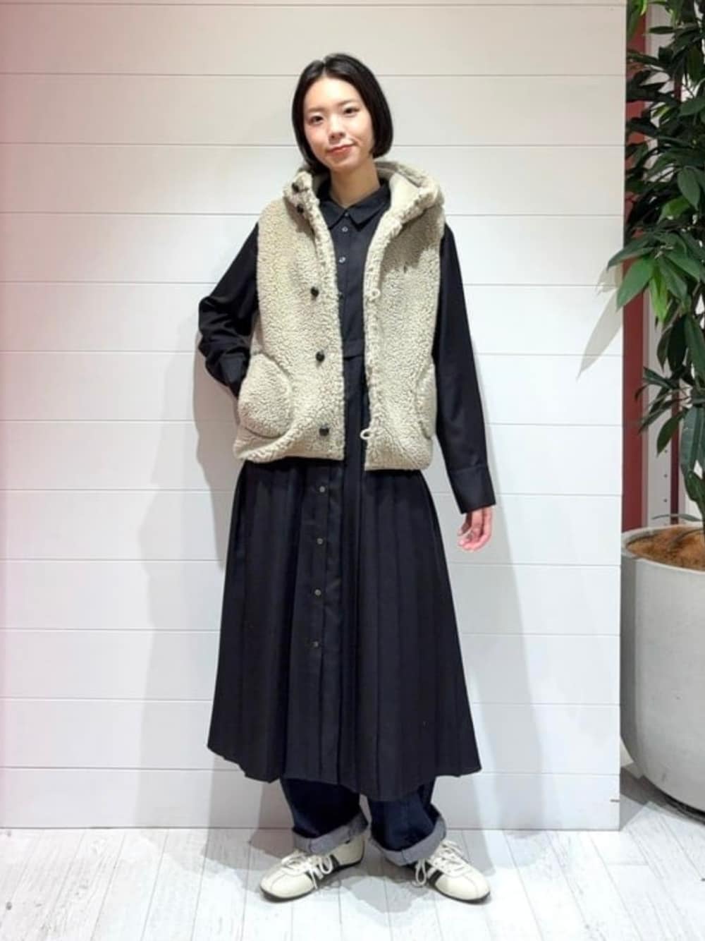ブルー系のデニムパンツ、ベージュ系のベスト、ブラック系のワンピースを着用したレディースの秋コーディネートの1枚目の写真