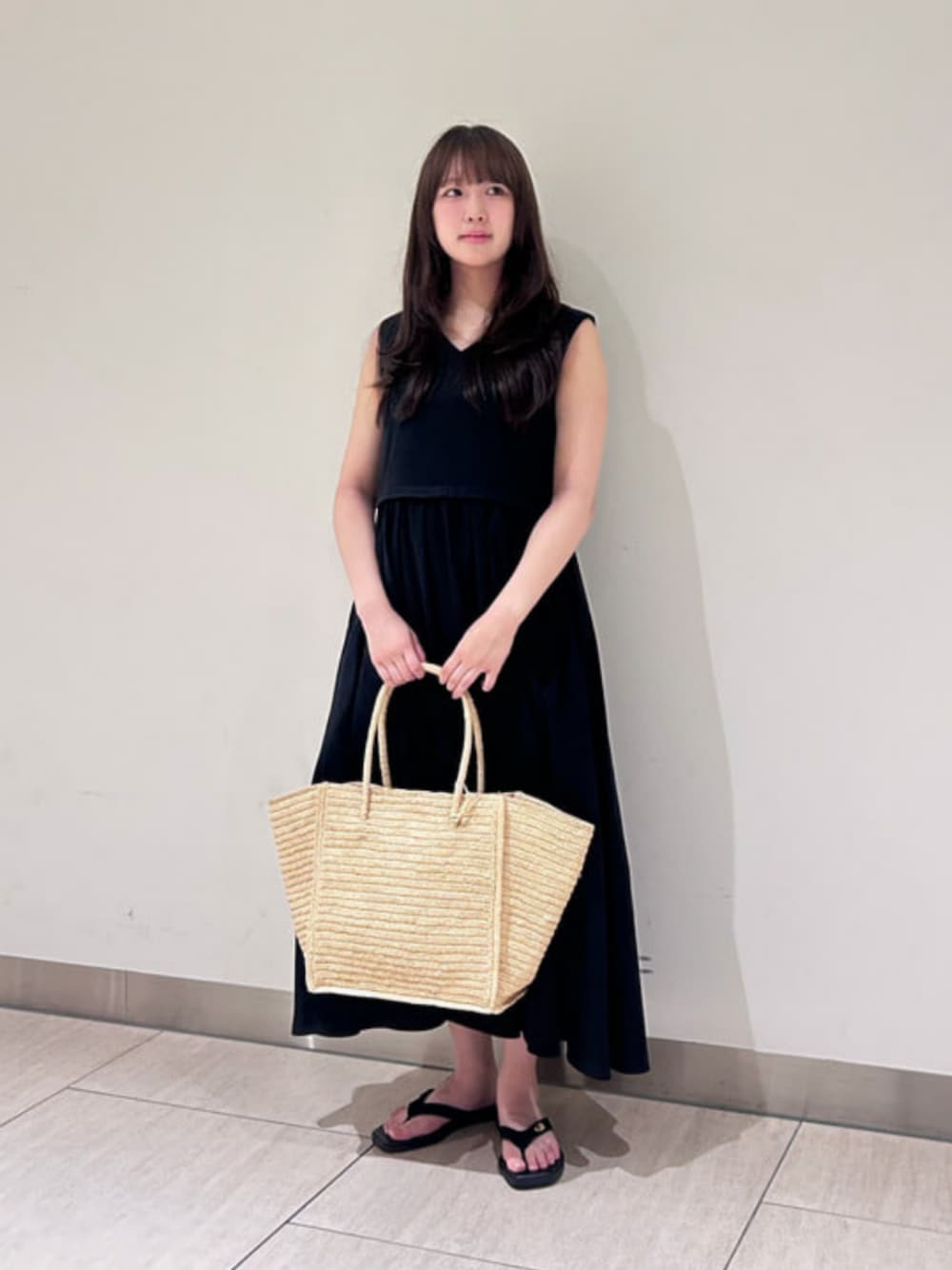 ブラック系のワンピース、ベージュ系のかごバッグ、ブラック系のサンダルを着用したレディースの夏コーディネートの1枚目の写真