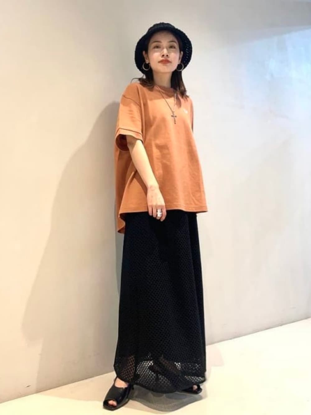 オレンジ系のTシャツ/カットソー、ブラック系のサンダル、ブラック系のハットを着用したレディースの春コーディネートの1枚目の写真