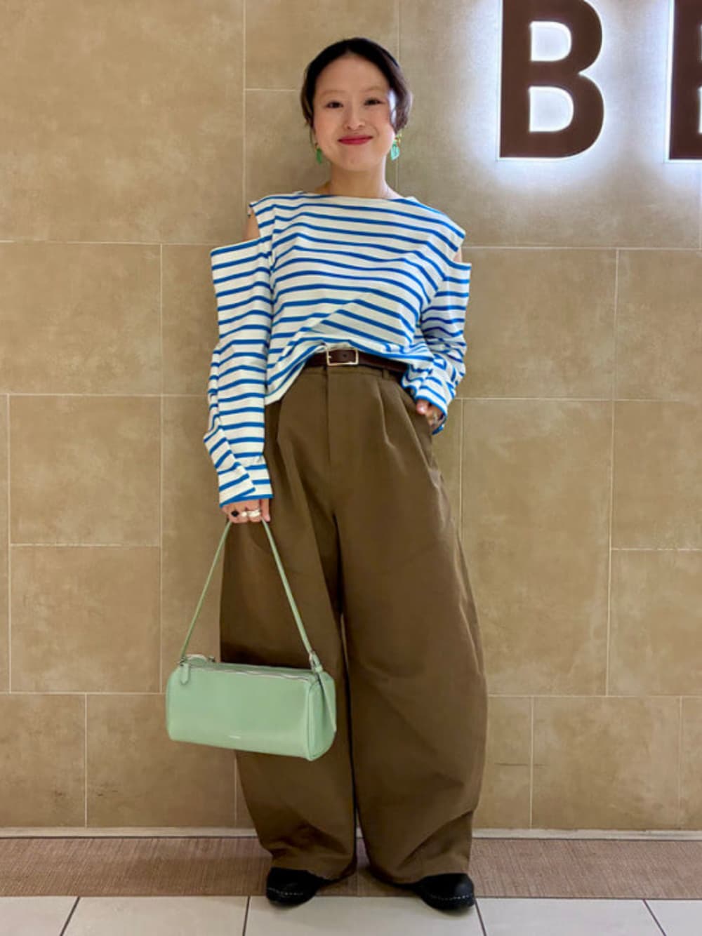 グリーン系のトートバッグ、ブラウン系のチノパンツ、ブルー系のTシャツ/カットソーを着用したレディースの春コーディネートの1枚目の写真