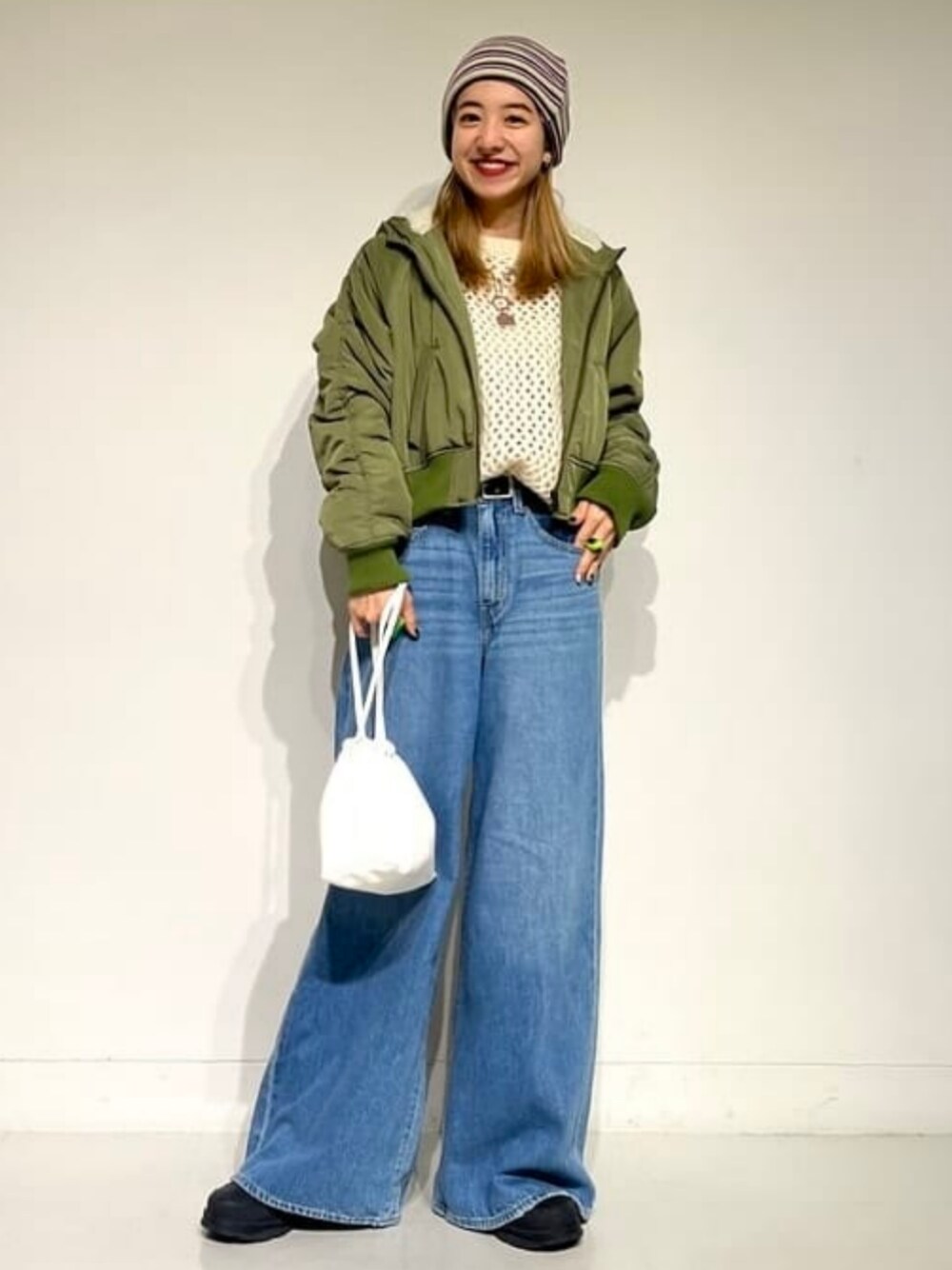 ホワイト系のニット/セーター、グリーン系のブルゾン、ブルー系のデニムパンツを着用したレディースの冬コーディネートの1枚目の写真