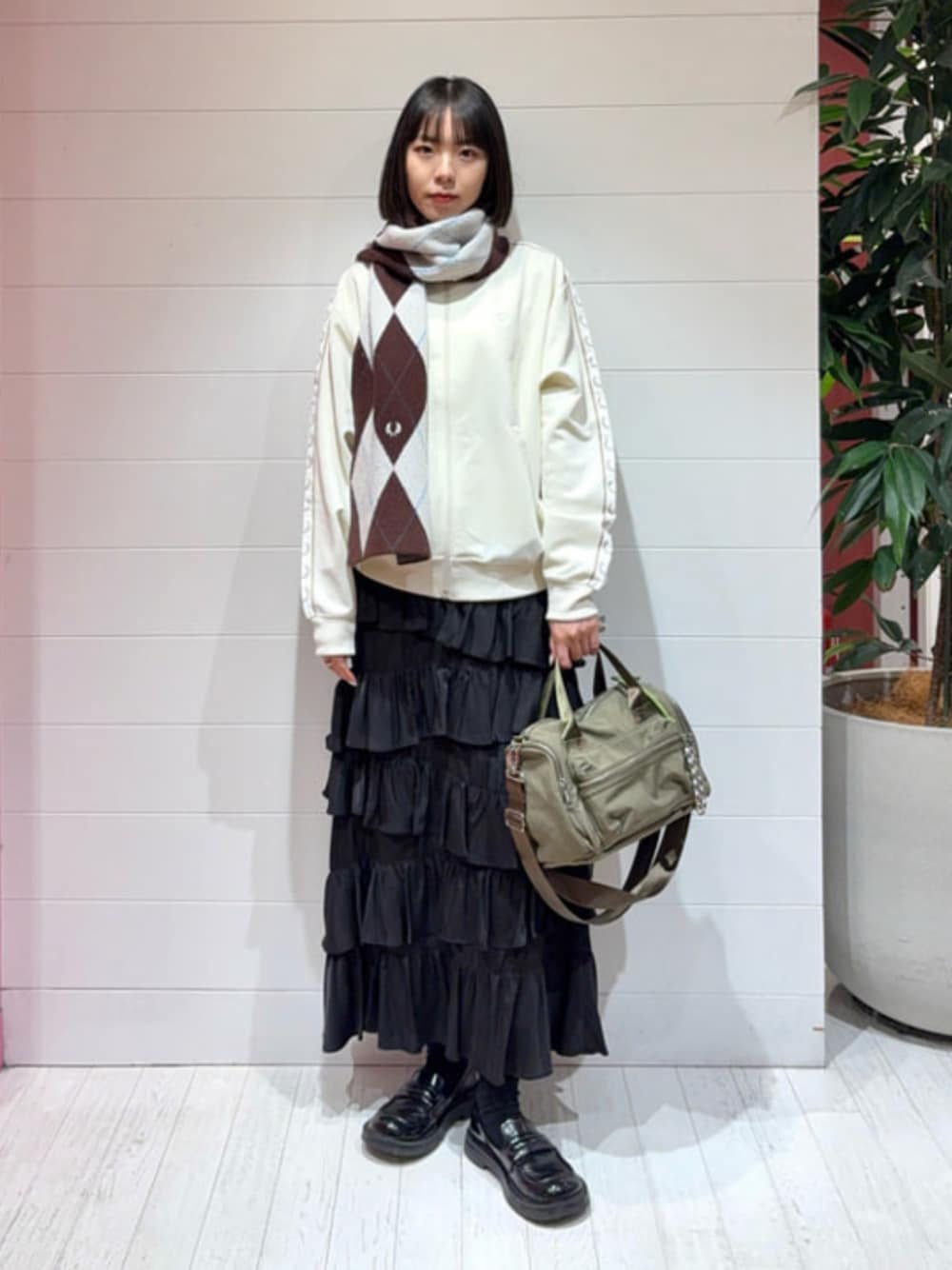 ホワイト系のジャージ、ブラック系のスカート、グリーン系のトートバッグを着用したレディースの冬コーディネートの1枚目の写真