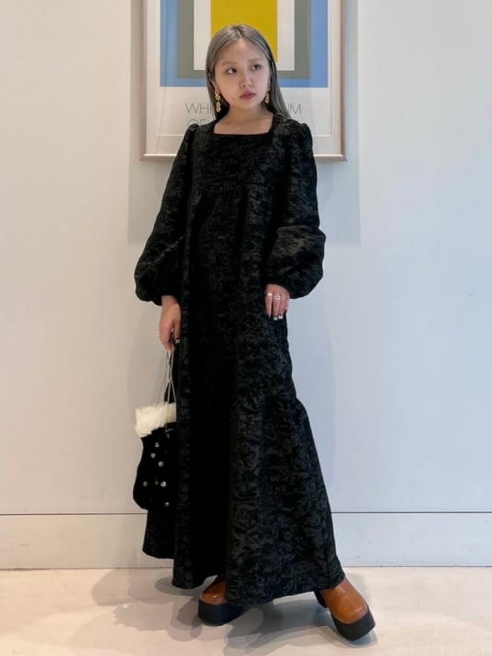 ブラック系のハンドバッグ、ブラック系のワンピース、ブラウン系のブーツを着用したレディースの秋コーディネートの1枚目の写真