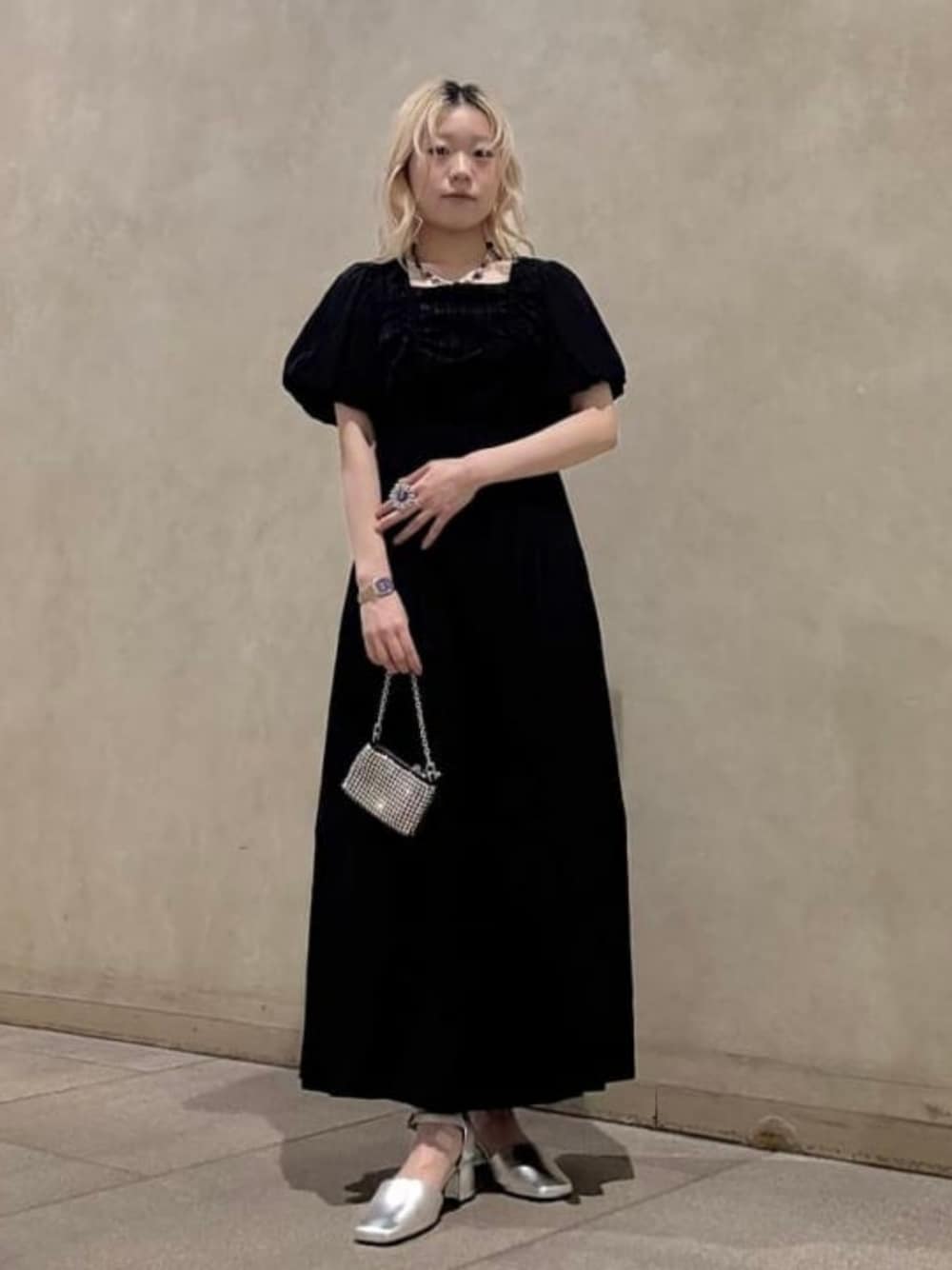 シルバー系のパンプス、ブラック系のワンピース、シルバー系のポーチを着用したレディースの春コーディネートの1枚目の写真