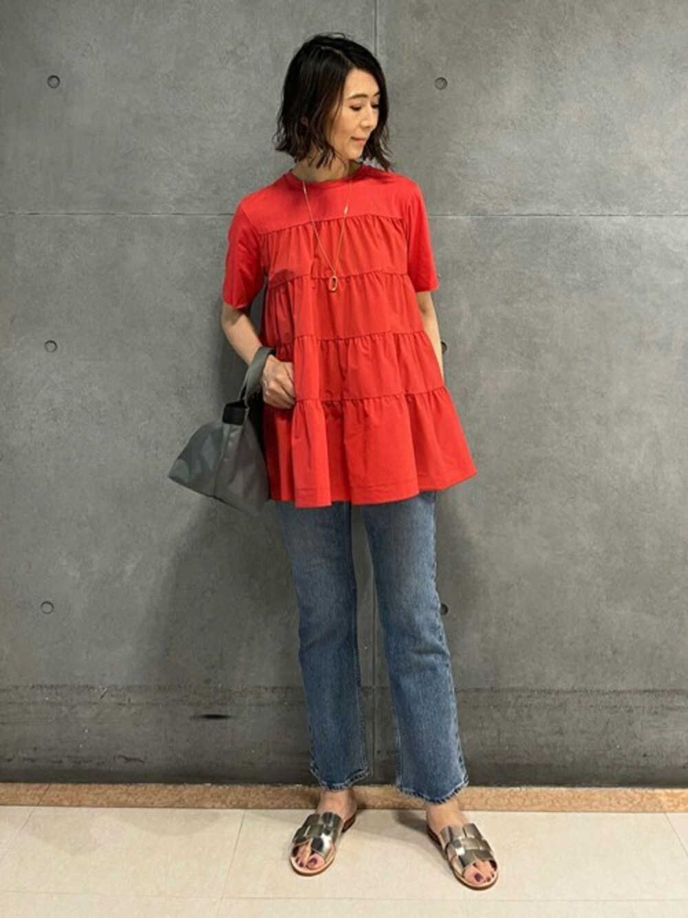 レッド系のTシャツ/カットソー、ブルー系のデニムパンツ、ゴールド系のサンダルを着用したレディースの夏コーディネートの1枚目の写真