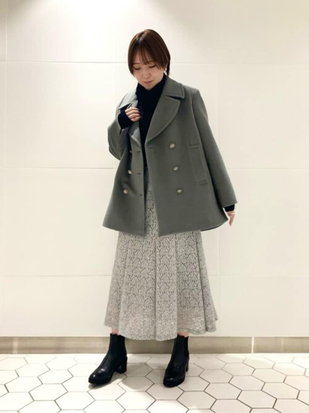 グリーン系のピーコート、ブルー系のニット/セーター、グレー系のスカートを着用したレディースの冬コーディネートの1枚目の写真