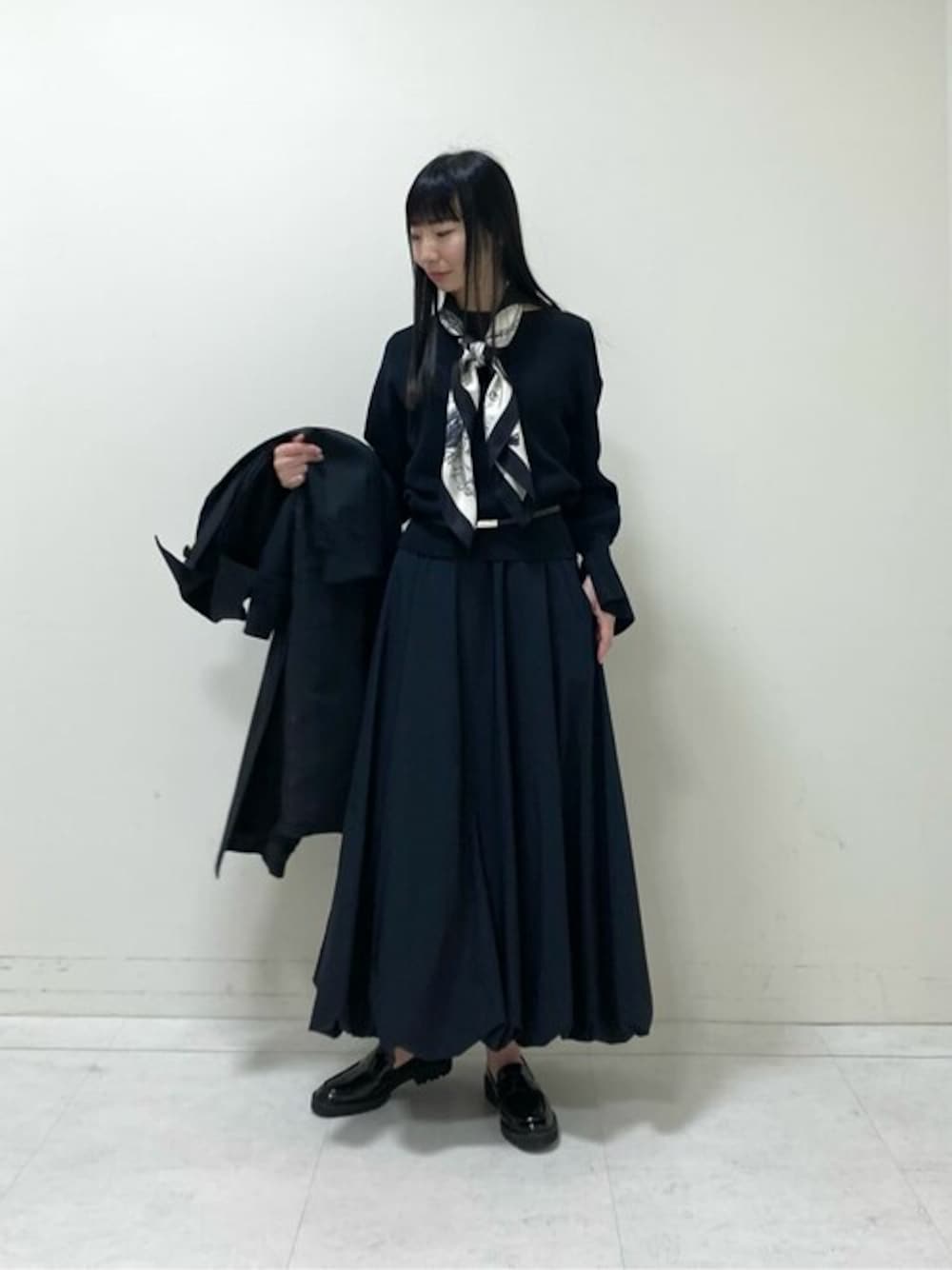 ブラック系のステンカラーコート、ブラック系のニット/セーター、ブラック系のスカートを着用したレディースの春コーディネートの1枚目の写真