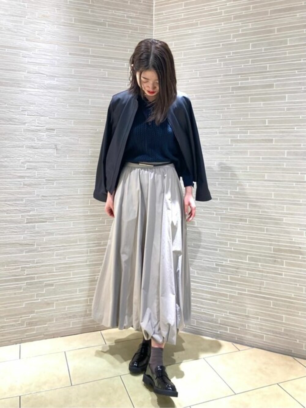 ブルー系のニット/セーター、ベージュ系のスカート、ブラック系のその他シューズを着用したレディースの春コーディネートの1枚目の写真