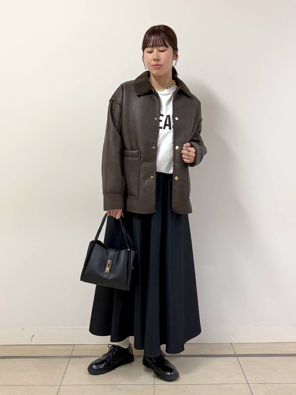 ブラウン系のムートンコート、ホワイト系のTシャツ/カットソー、ブラック系のハンドバッグを着用したレディースの秋コーディネートの1枚目の写真