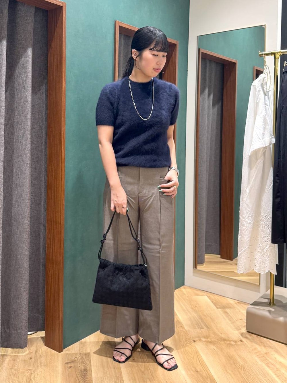 ブラック系のショルダーバッグ、ブルー系のニット/セーター、ベージュ系のスラックスを着用したレディースの夏コーディネートの1枚目の写真