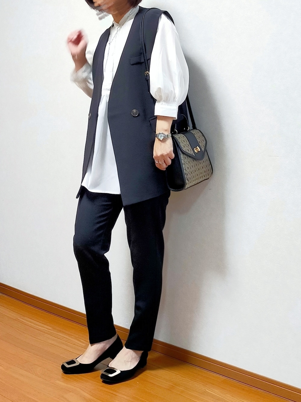 ブラック系のベスト、ブラック系のスラックス、ブラック系のパンプスを着用したレディースの春コーディネートの1枚目の写真