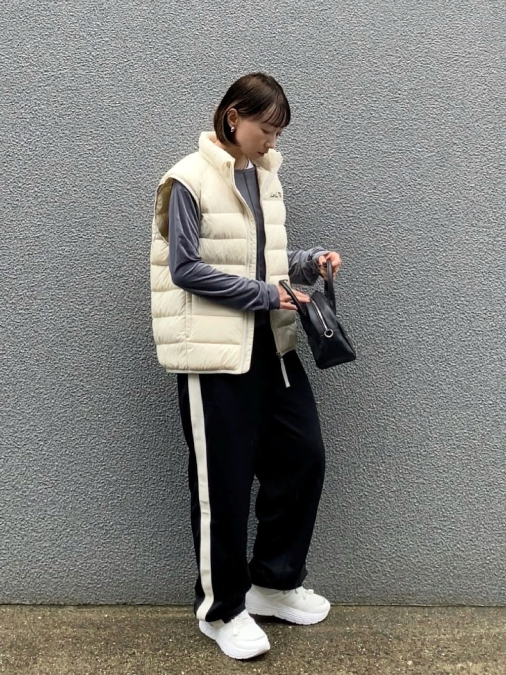 グレー系のTシャツ/カットソー、ホワイト系のダウンベスト、ブラック系のボストンバッグを着用したレディースの秋コーディネートの1枚目の写真