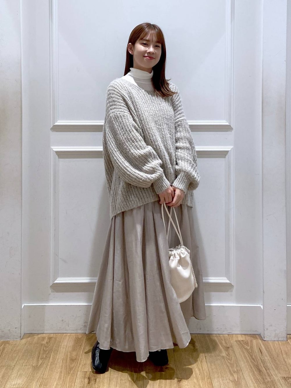 ホワイト系のショルダーバッグ、ベージュ系のスカート、ブラック系のブーツを着用したレディースの冬コーディネートの1枚目の写真