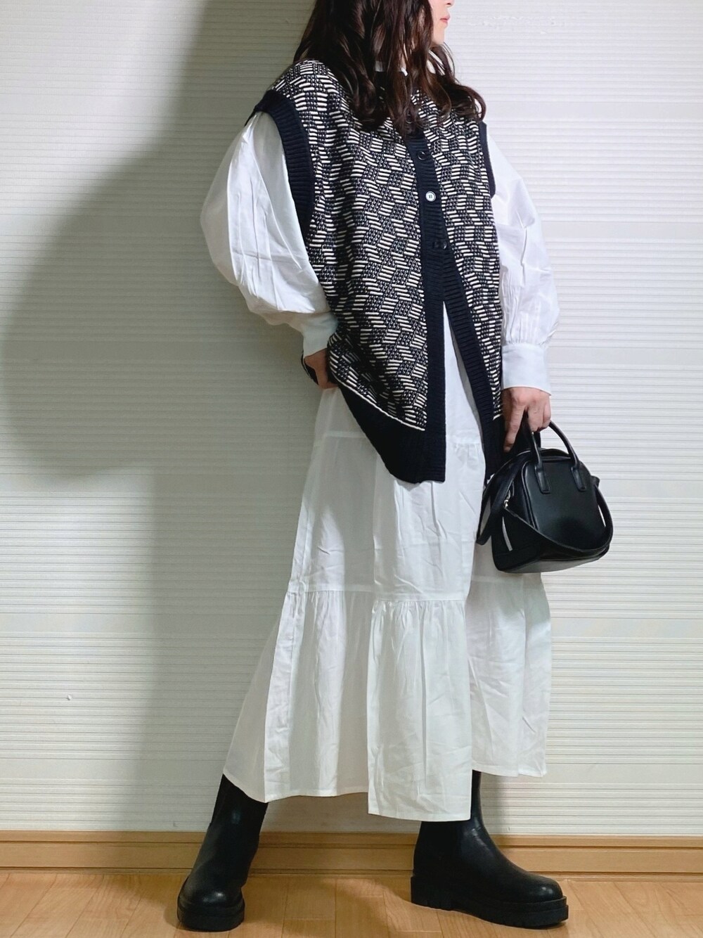 ブラック系のベスト、グリーン系のワンピース、ブラック系のハンドバッグを着用したレディースの秋コーディネートの1枚目の写真