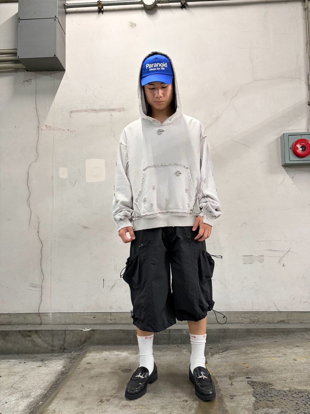 ホワイト系のパーカー、ブラック系のパンツ、ブルー系のキャップを着用したメンズの夏コーディネートの1枚目の写真