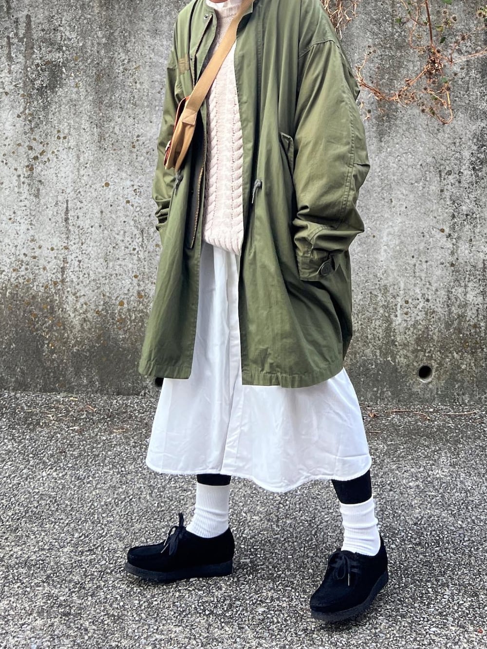 グリーン系のミリタリージャケット、ホワイト系のニット/セーター、ベージュ系のショルダーバッグを着用したレディースの冬コーディネートの1枚目の写真