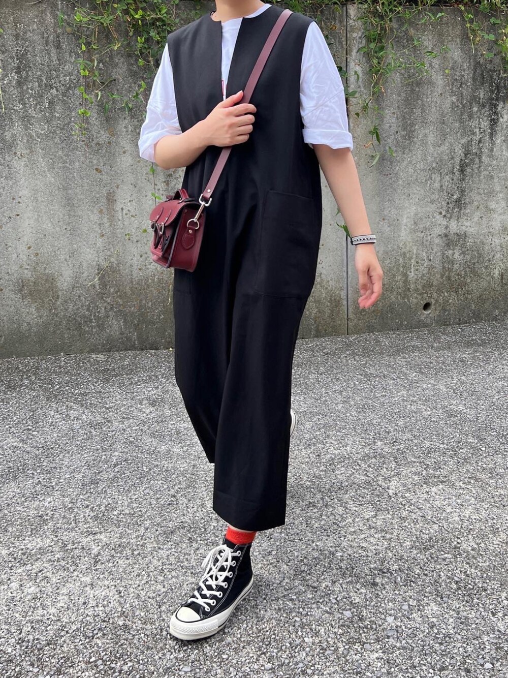 ブラウン系のショルダーバッグ、ブラック系のジャンパースカート、ブラック系のスニーカーを着用したレディースの秋コーディネートの1枚目の写真