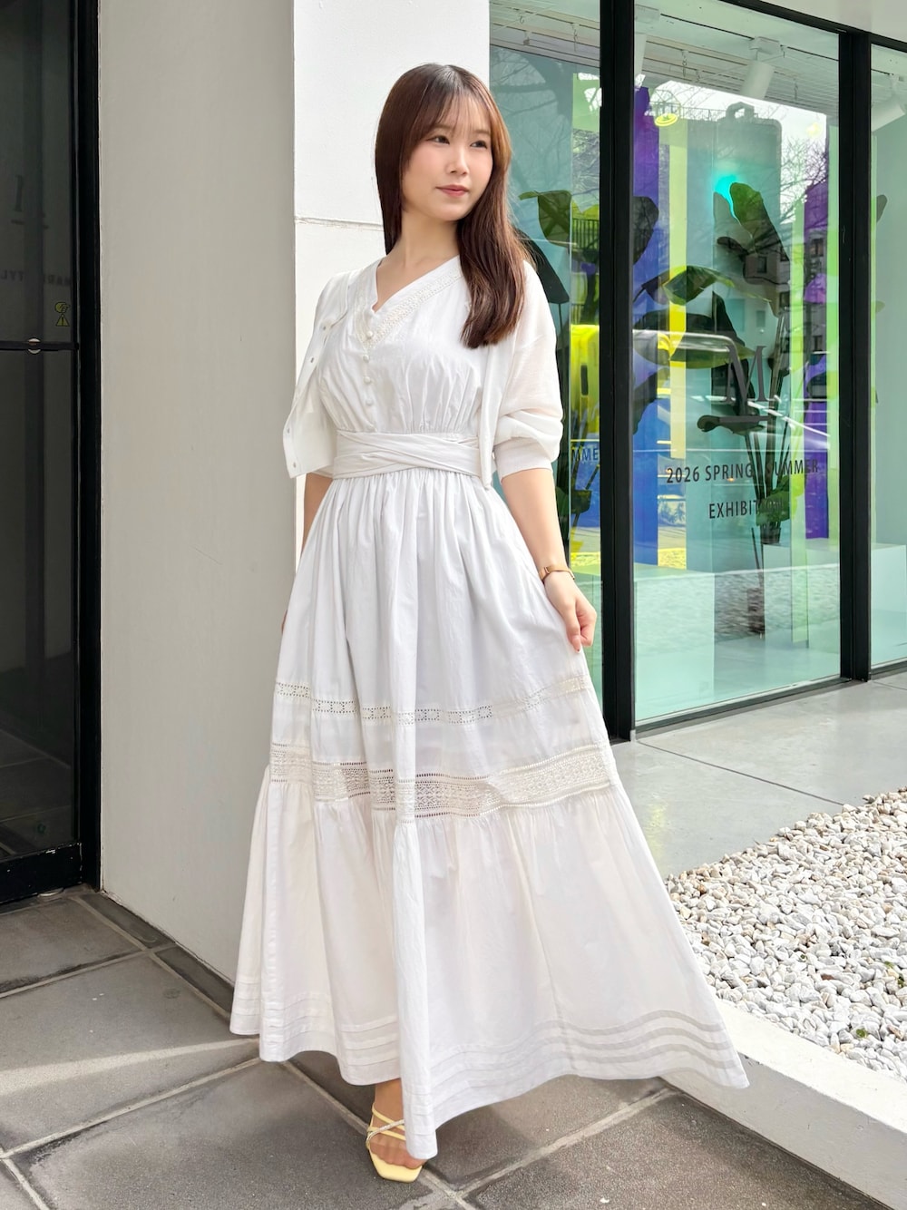 ホワイト系のワンピース、ホワイト系のカーディガン/ボレロ、イエロー系のサンダルを着用したレディースの春コーディネートの1枚目の写真