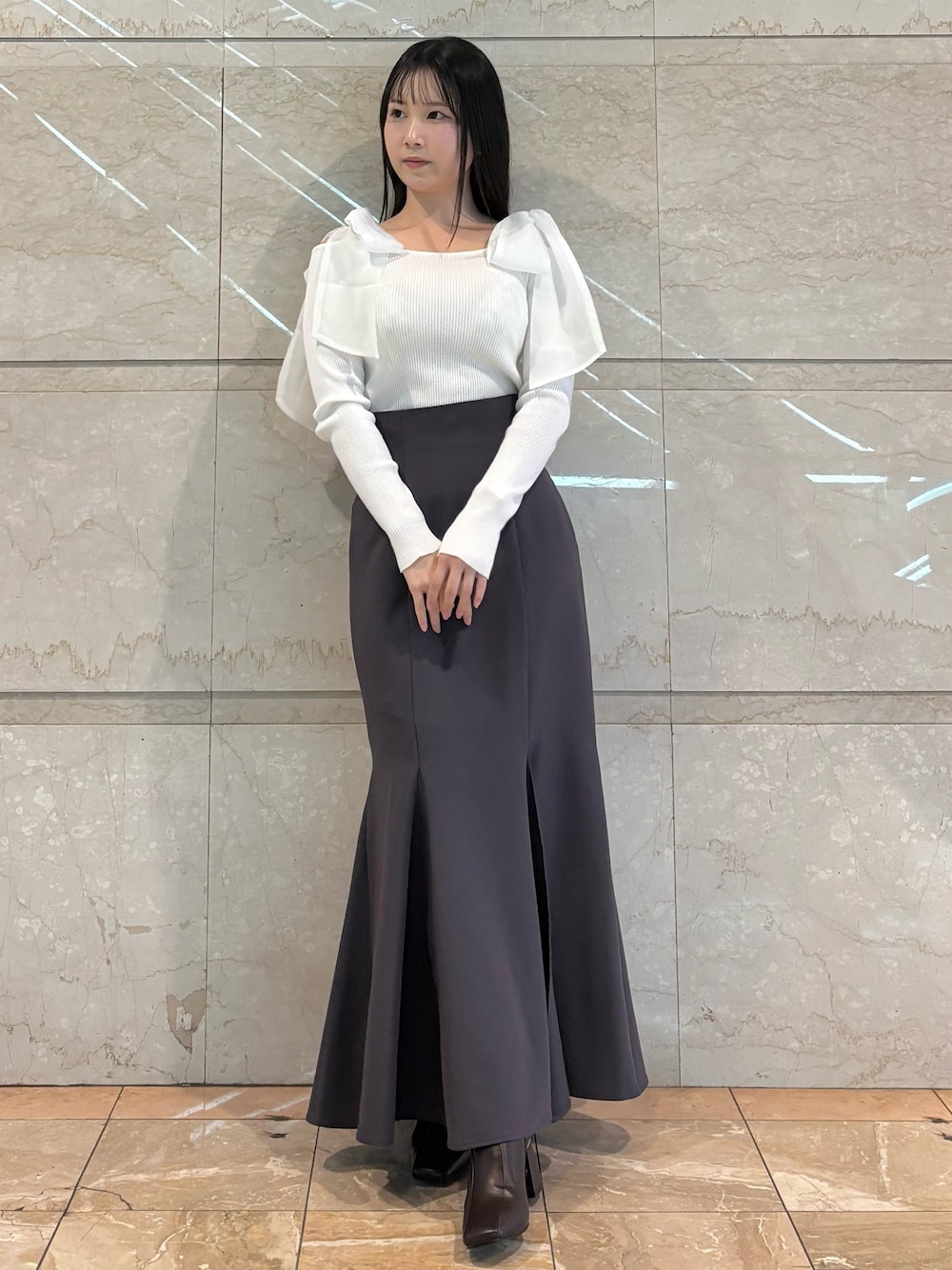 グレー系のスカート、ブラウン系のブーツ、ホワイト系のニット/セーターを着用したレディースの冬コーディネートの1枚目の写真