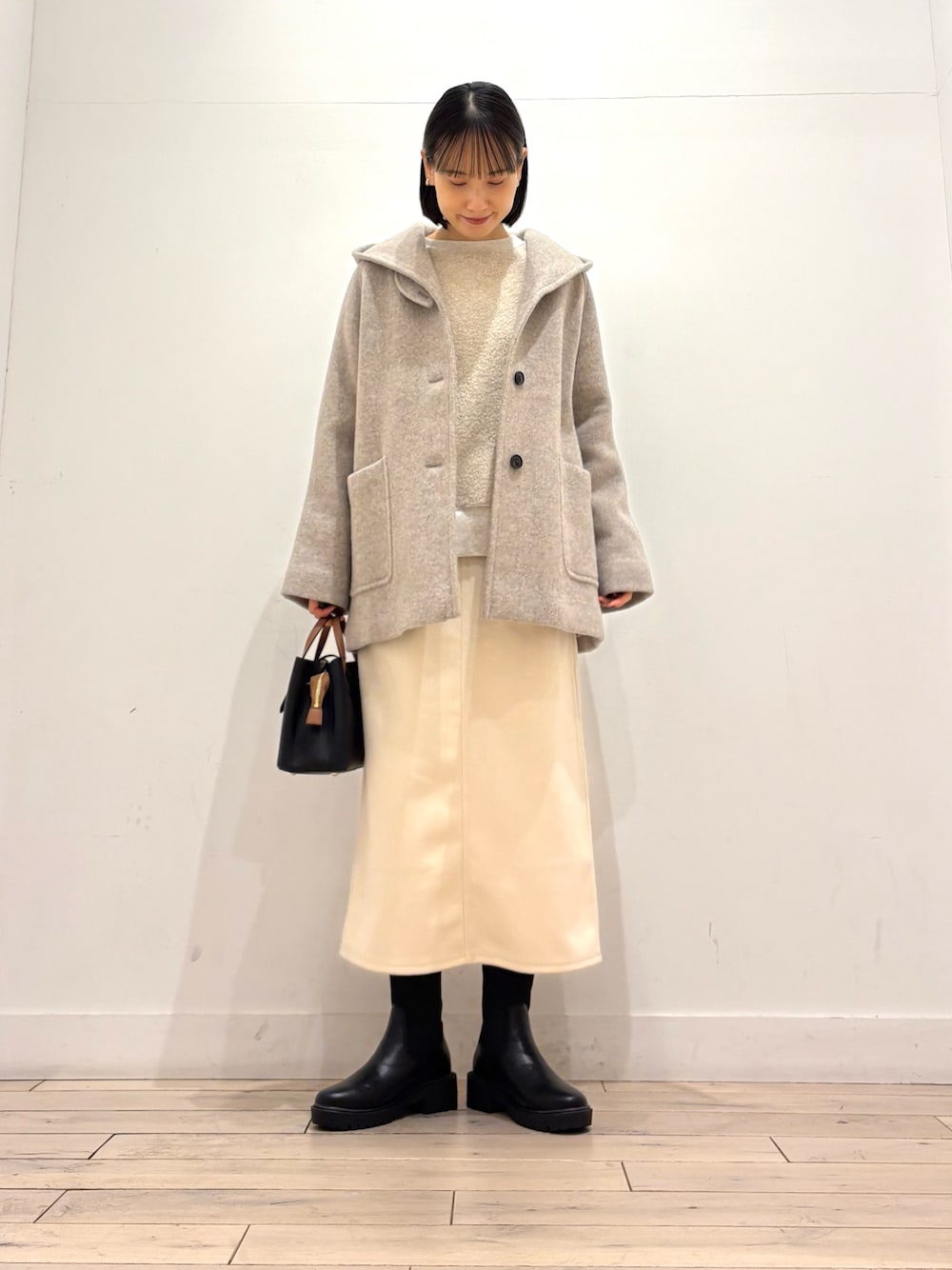 ブラック系のブーツ、ブラック系のハンドバッグ、ホワイト系のスカートを着用したレディースの冬コーディネートの1枚目の写真