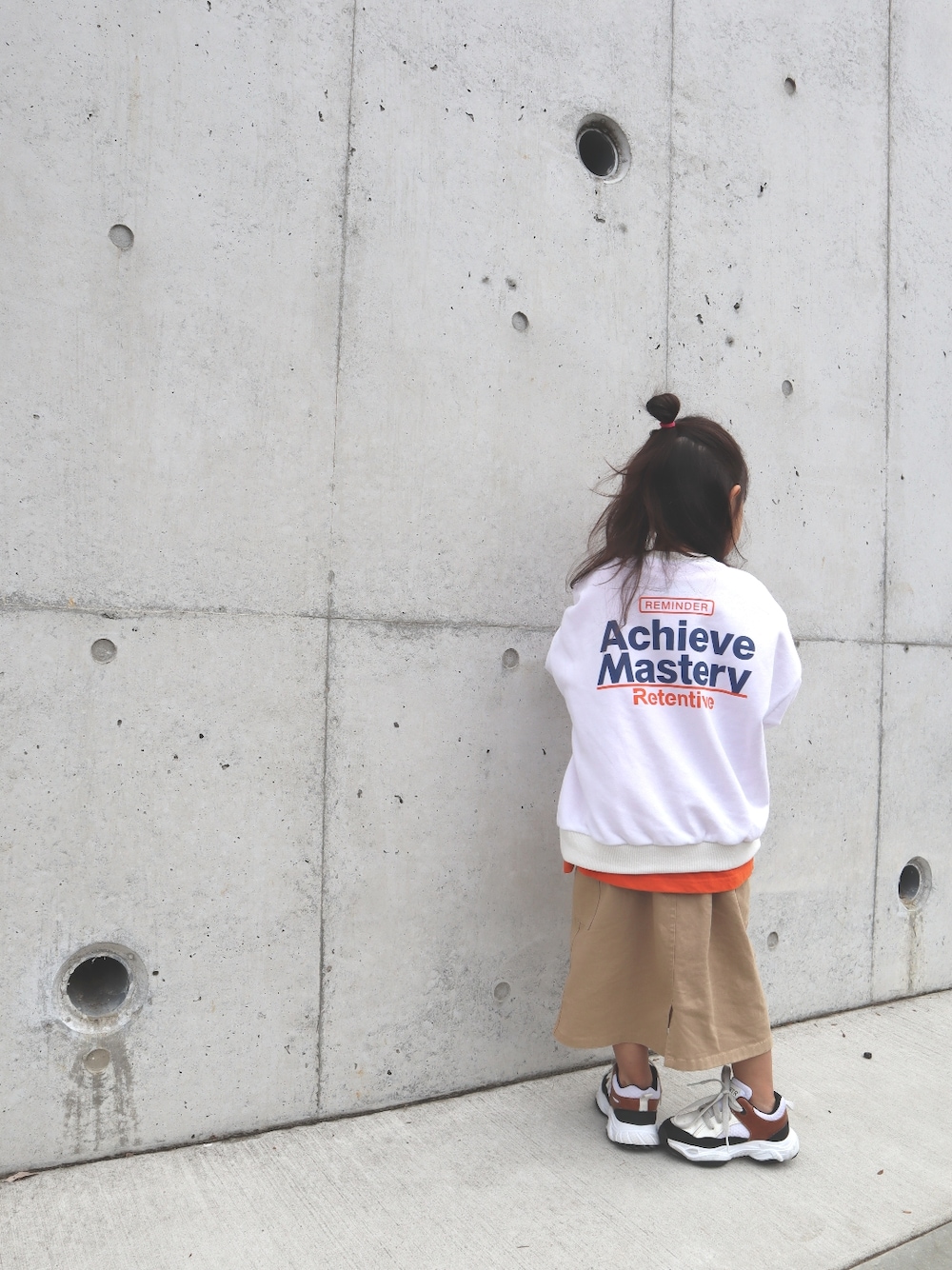 ホワイト系のスウェット、オレンジ系のTシャツ/カットソー、ベージュ系のスカートを着用したキッズの春コーディネートの3枚目の写真