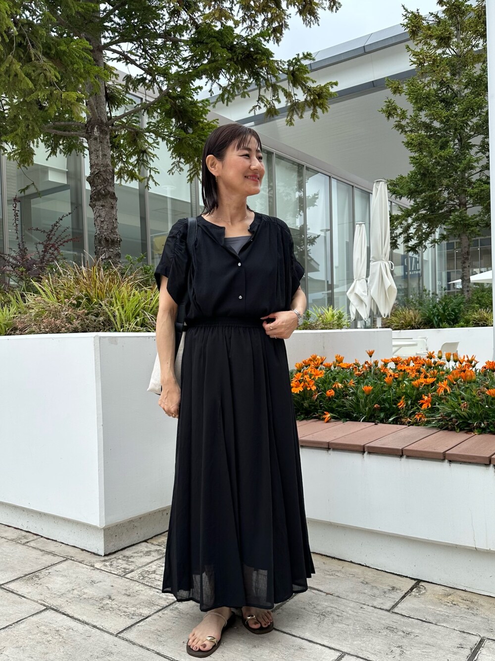 ブラック系のシャツ/ブラウス、ブラック系のスカート、ゴールド系のネックレスを着用したレディースの夏コーディネートの1枚目の写真