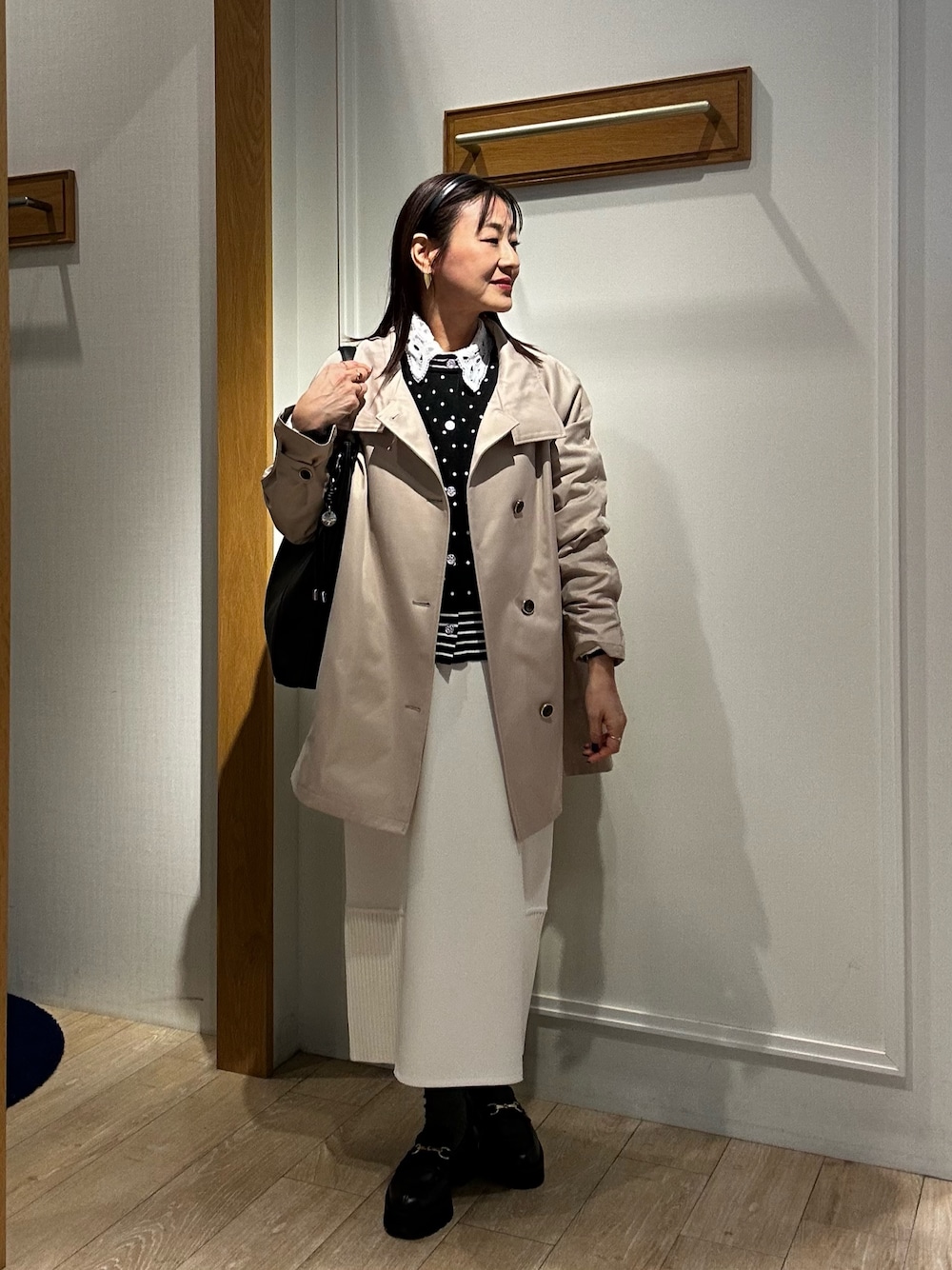 ベージュ系のその他アウター、ブラック系のニット/セーター、ホワイト系のスカートを着用したレディースの冬コーディネートの1枚目の写真