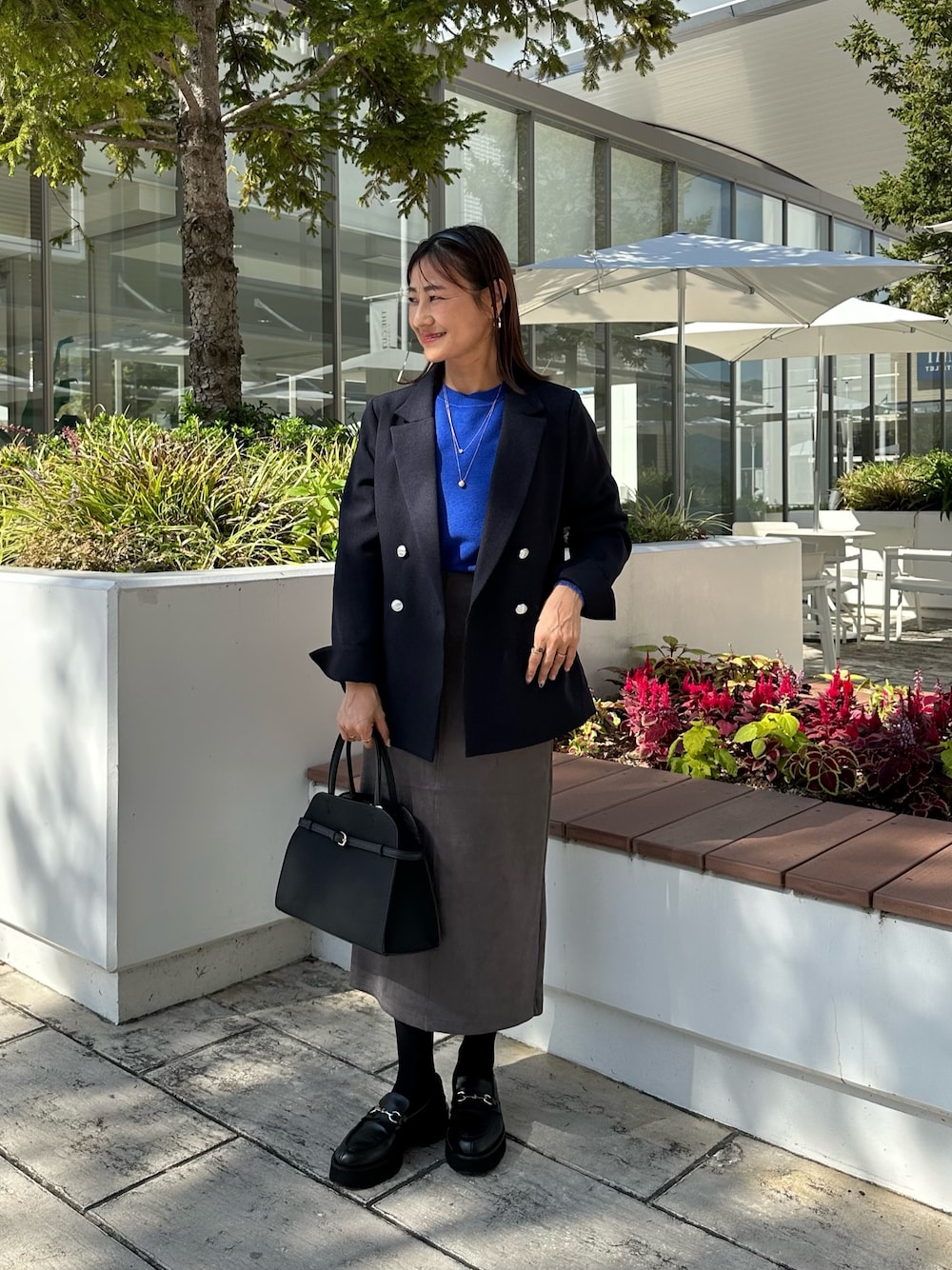 ブルー系のテーラードジャケット、ブルー系のニット/セーター、グレー系のスカートを着用したレディースの秋コーディネートの1枚目の写真