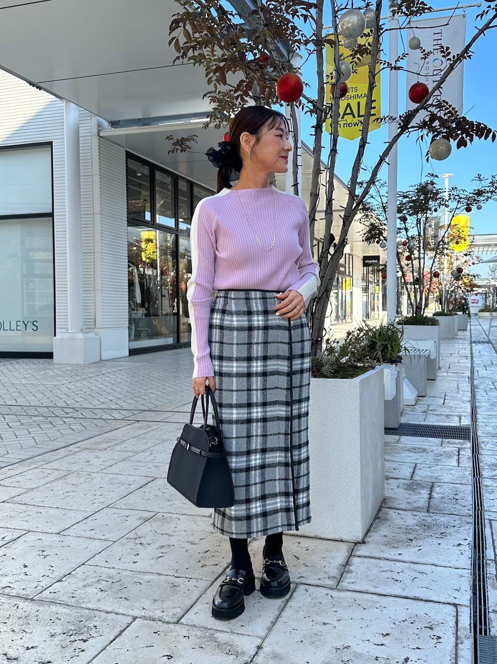 グレー系のスカート、ブラック系のトートバッグ、ピンク系のニット/セーターを着用したレディースの秋コーディネートの1枚目の写真