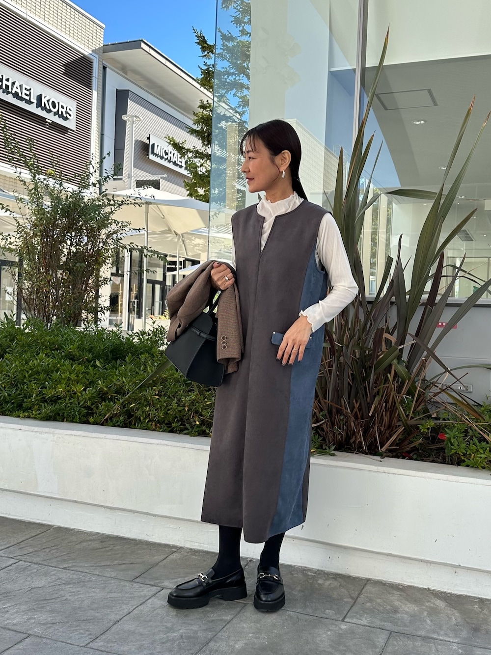 グレー系のワンピース、ホワイト系のTシャツ/カットソー、ブラウン系のテーラードジャケットを着用したレディースの秋コーディネートの1枚目の写真