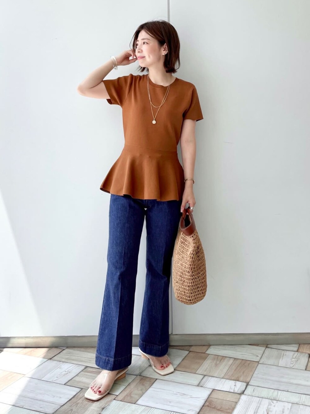 イエロー系のニット/セーター、ブルー系のデニムパンツ、ベージュ系のクラッチバッグを着用したレディースの夏コーディネートの1枚目の写真