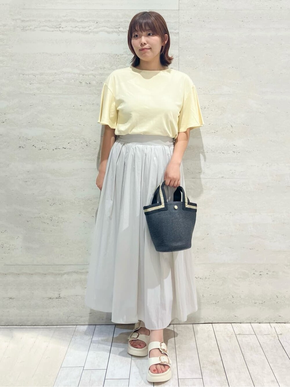 イエロー系のTシャツ/カットソー、グレー系のスカート、ブラック系のトートバッグを着用したレディースの夏コーディネートの1枚目の写真